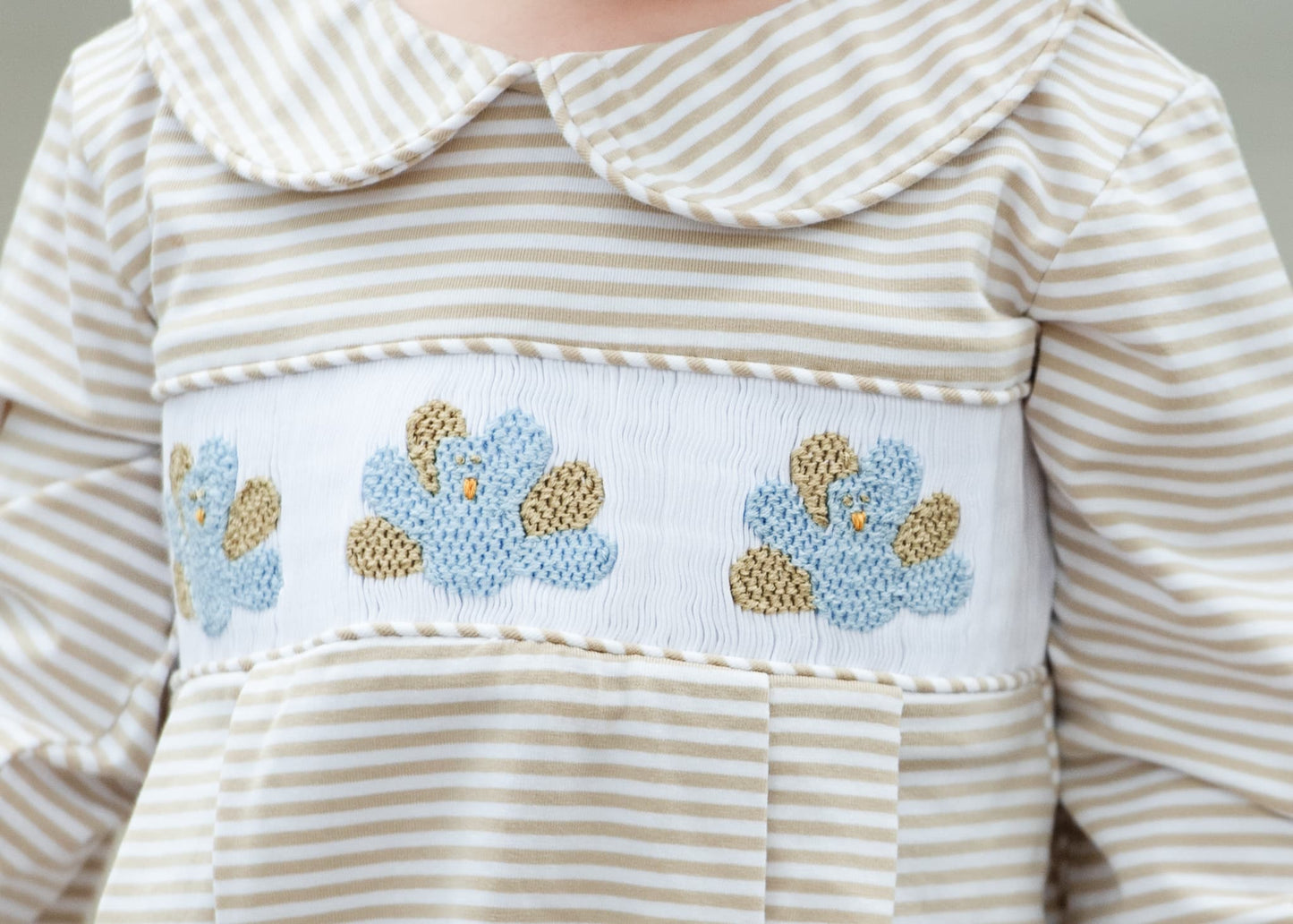 Close-up of a child's dress with striped pattern and floral embroidery.