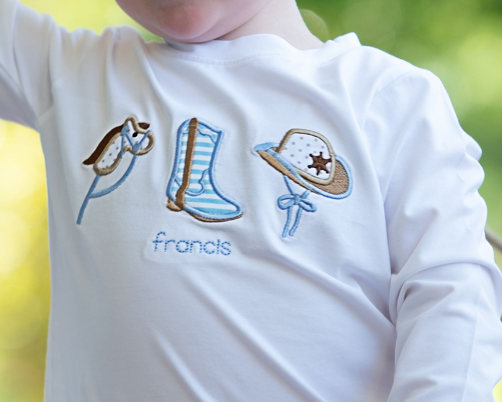Close-up of a child's shirt with embroidered cowboy design and 'francis' text.