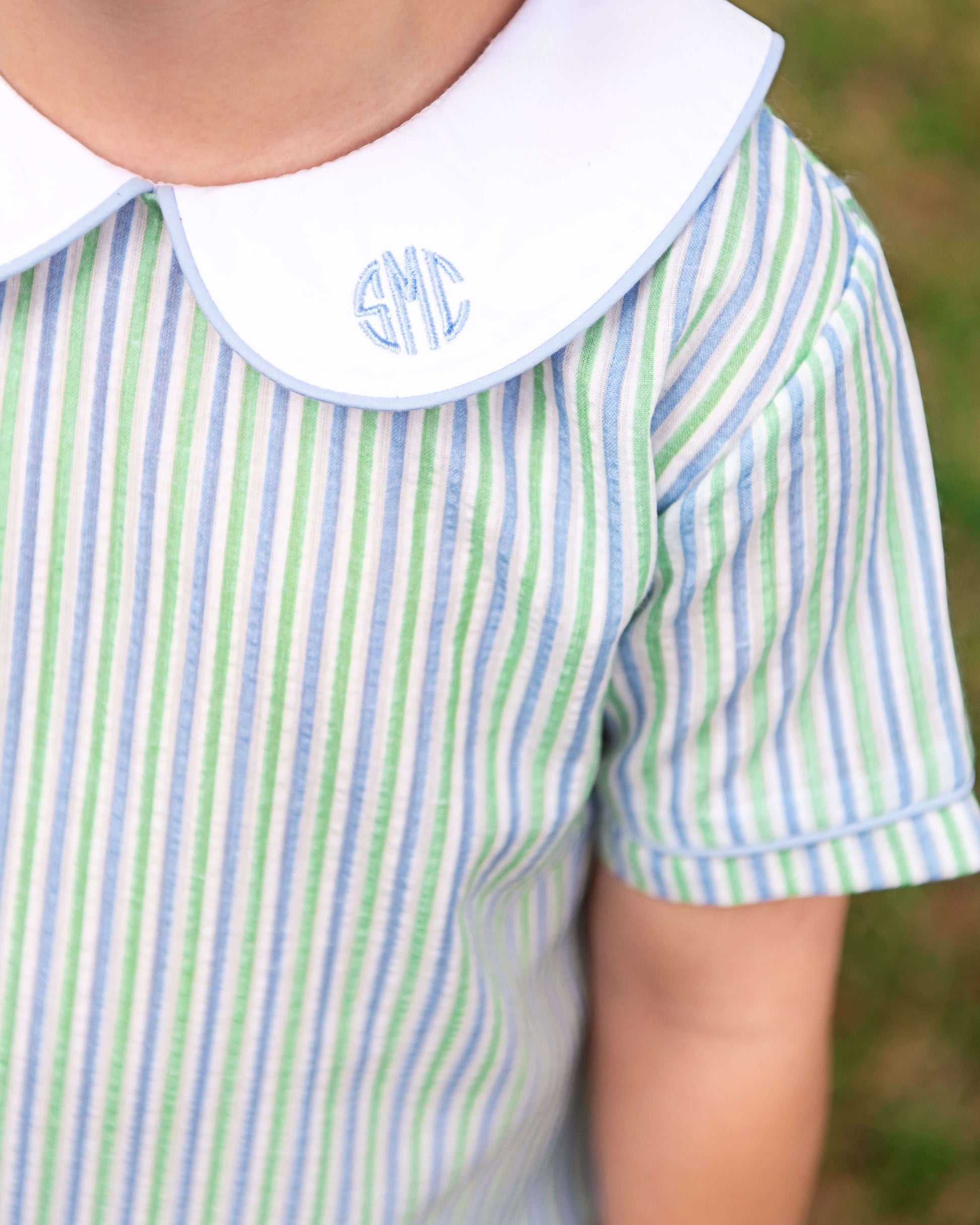 Close-up of a child's shirt with green and blue stripes and a white collar with monogram.