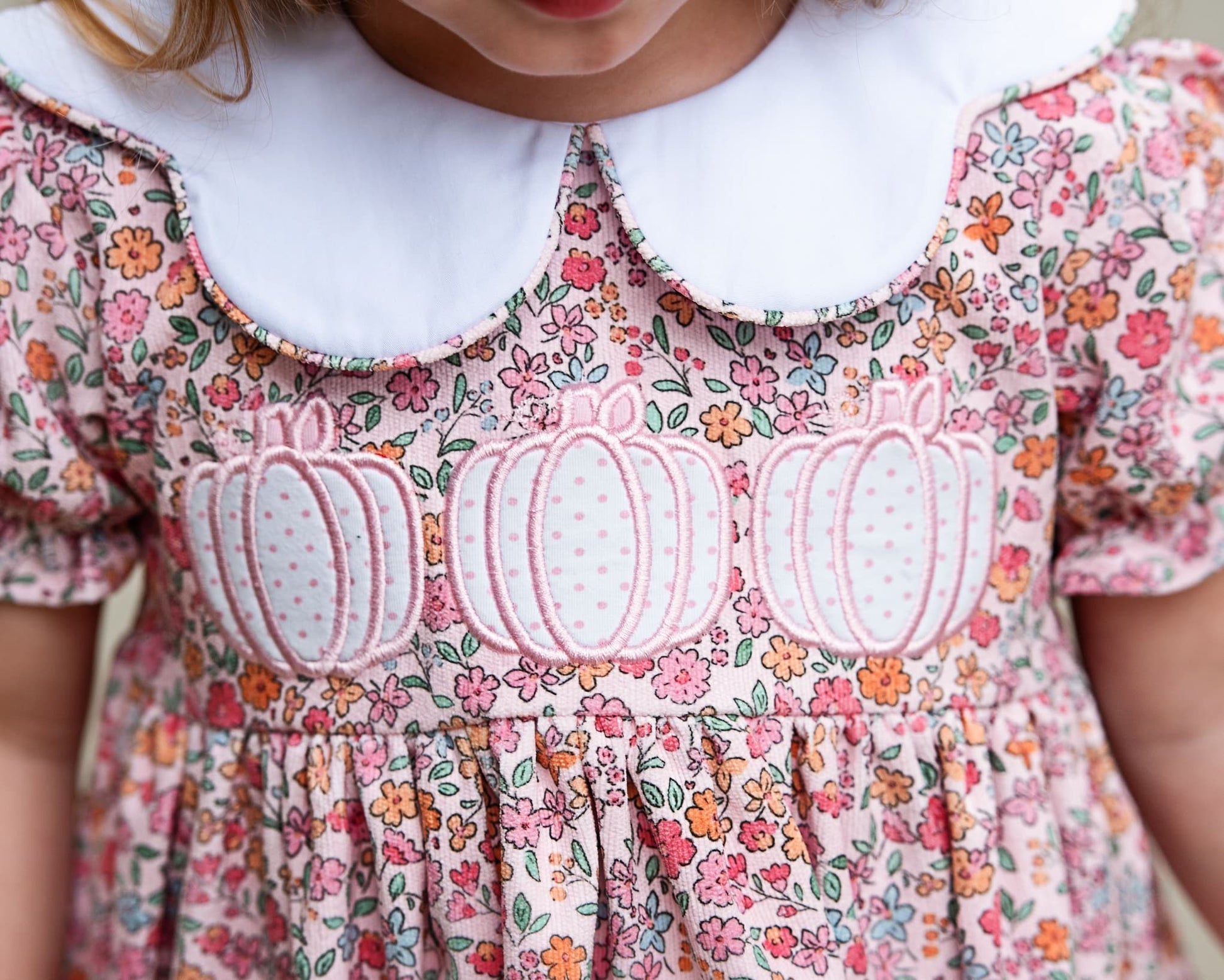 Close-up of a child wearing a floral pumpkin dress with a white collar.