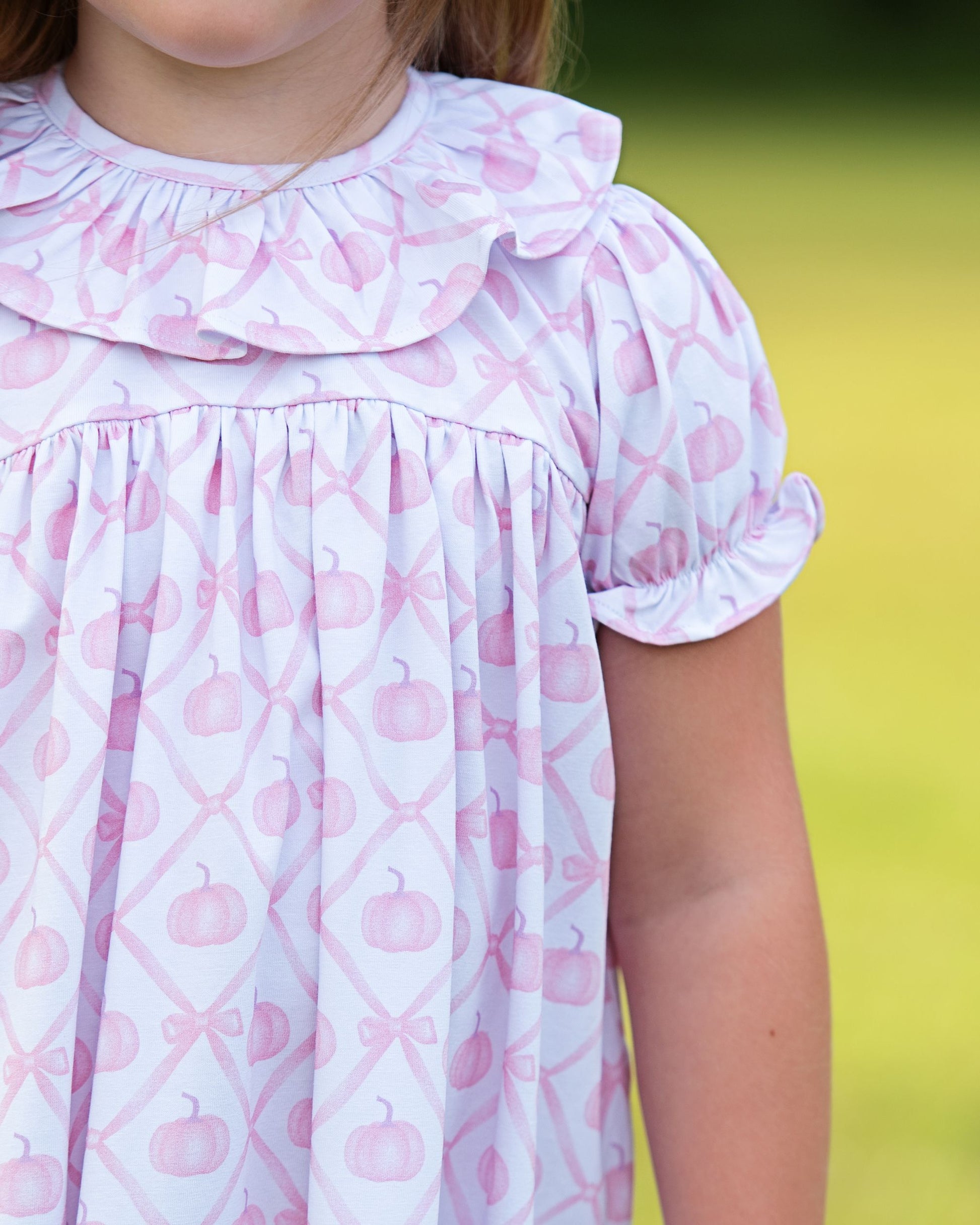Close-up of a child wearing a pink and white dress with pumpkin pattern against a blurred green background
