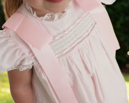 Close-up of a child wearing a pink dress with lace details against a blurred green background