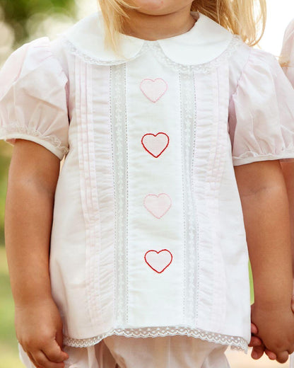 Close-up of a child wearing a white set with heart patterns.