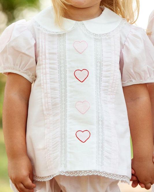 Close-up of a child wearing a white set with heart patterns.
