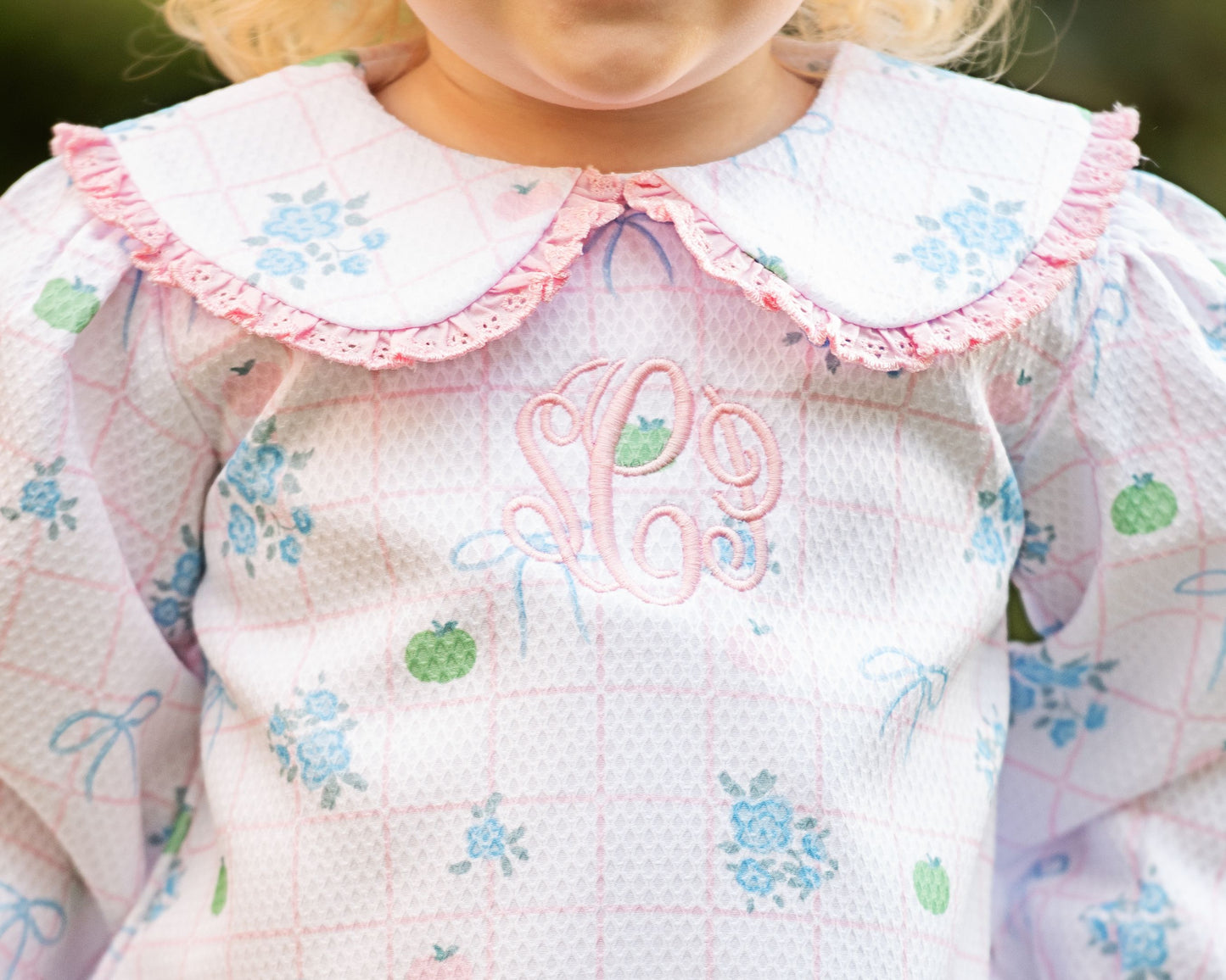 Close-up of a girl wearing a pumpkin legging set with a pink collar and embroidered initials.