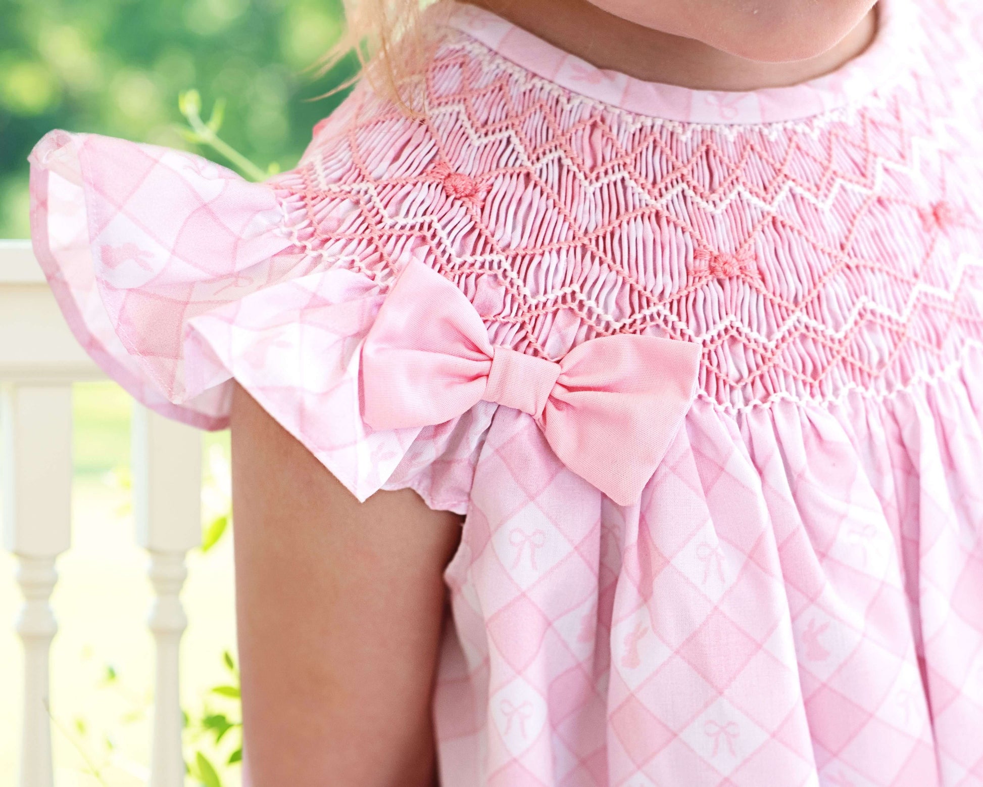 Close-up of a pink dress with a bow detail, blurred green background