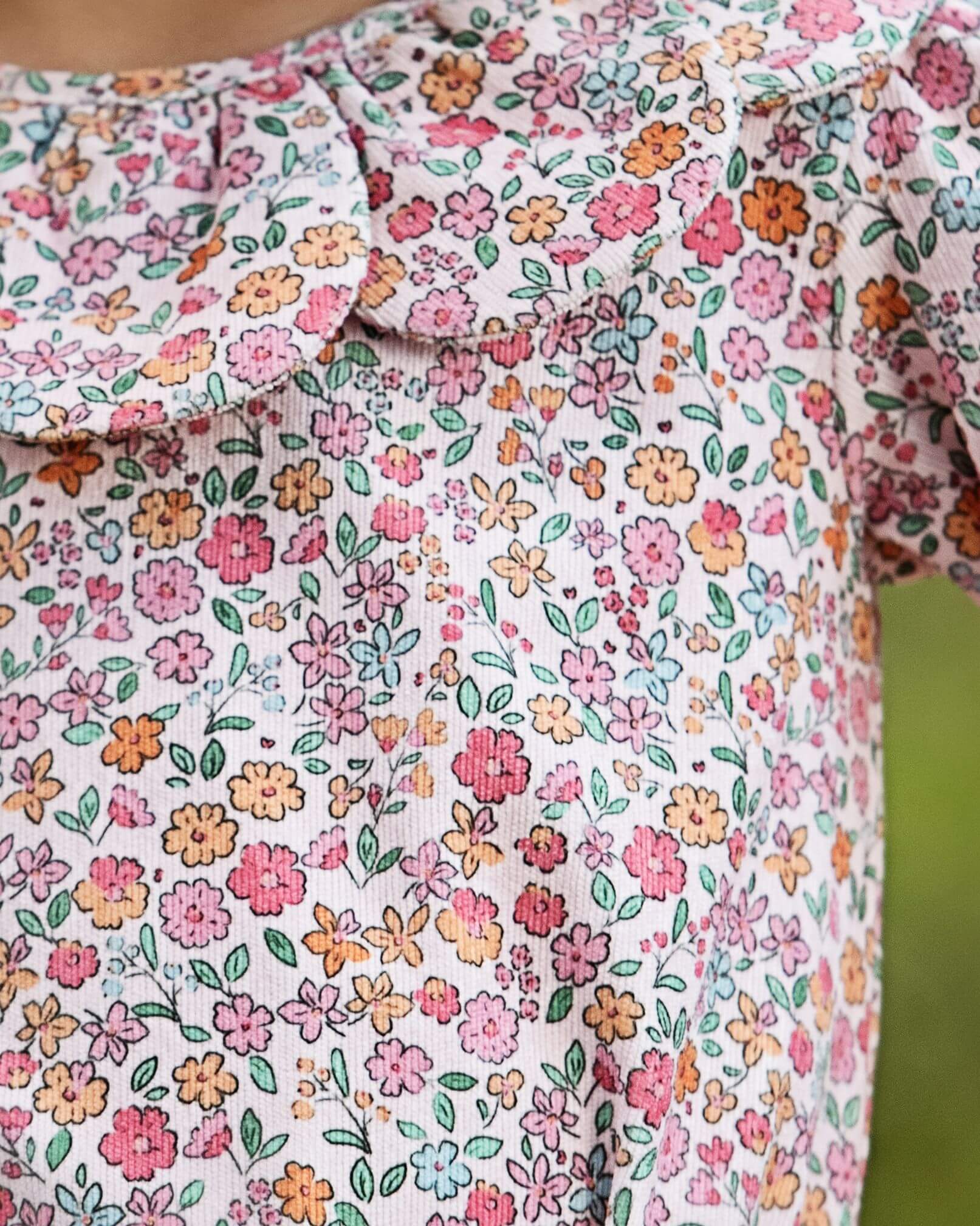 Close-up of a pink fabric with a dense multicolor floral print featuring pink, orange, yellow, and green flowers and leaves