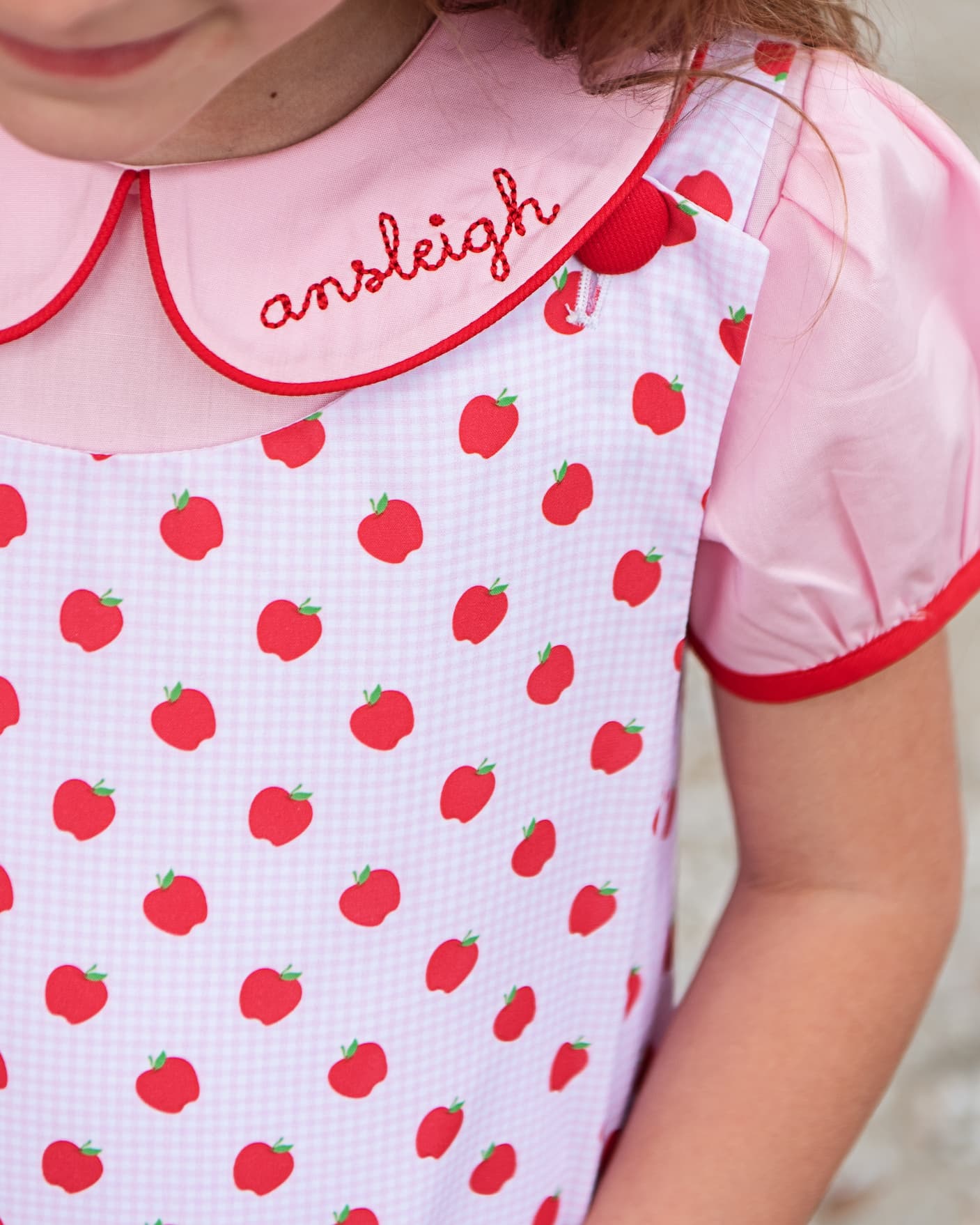 Close up of a pink apple print dress with the name ansleigh embroidered