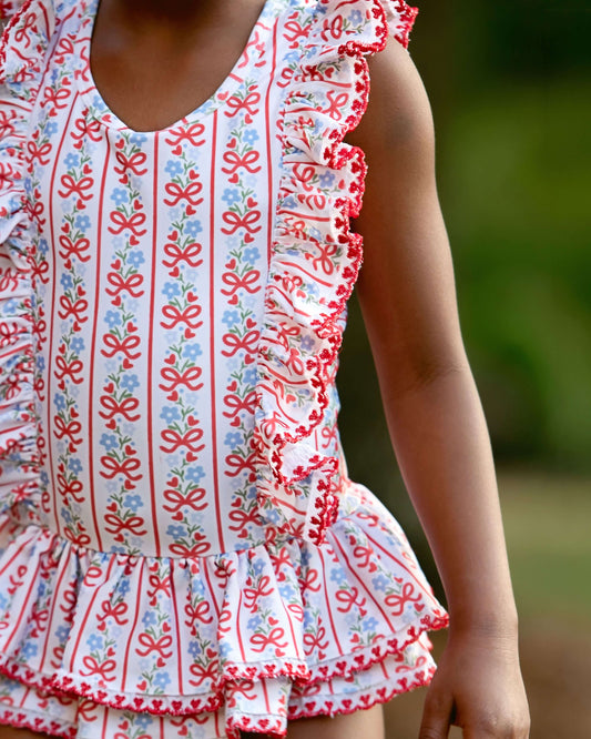 Close up of a red and blue floral and bow swimsuit with ruffle trim. 
