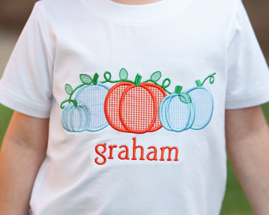 Close up of a white t shirt with a pumpkin applique and name " graham" embroidered on it 