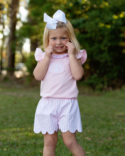 Young girl wearing a pink top with pink striped shorts standing on the grass