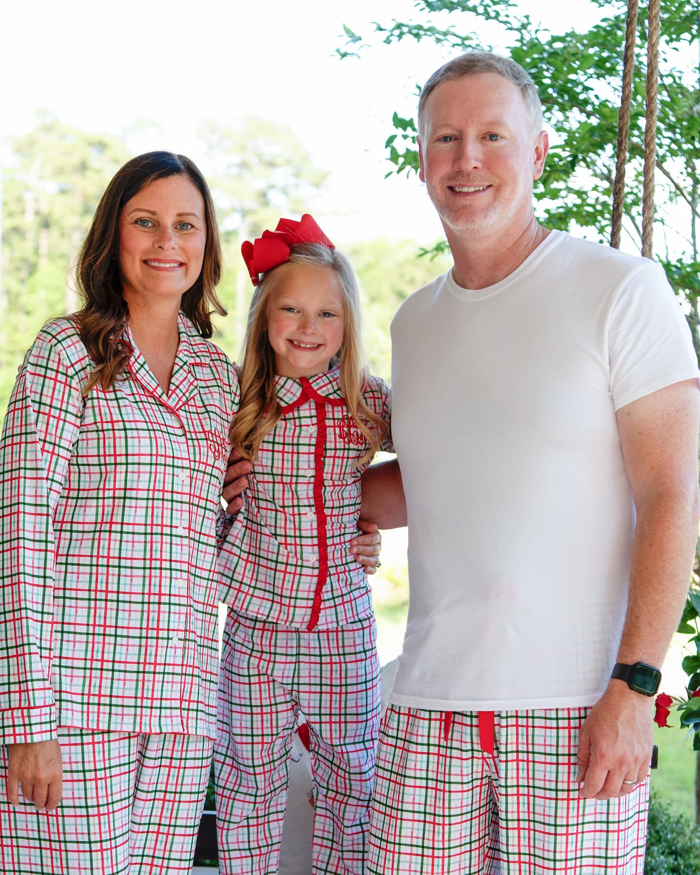 Family of three wearing matching red and white plaid pajamas outdoors.