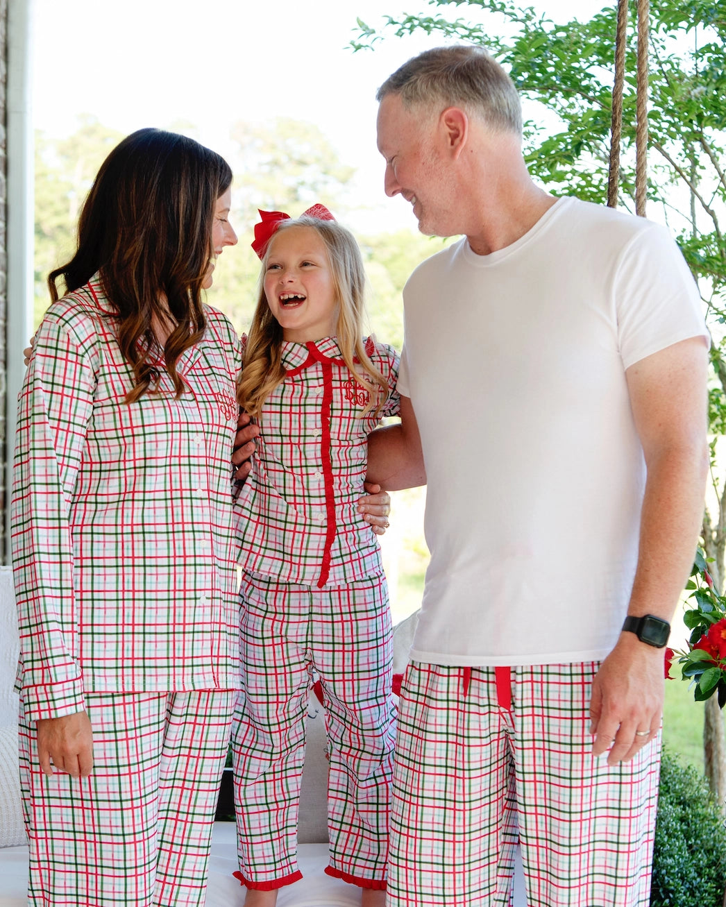 Family of three wearing matching red and white plaid pajamas outdoors.