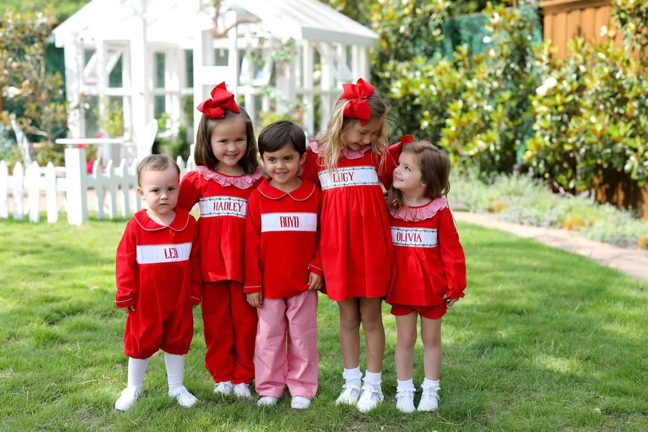 Five children in matching red outfits with name labels standing on grass.