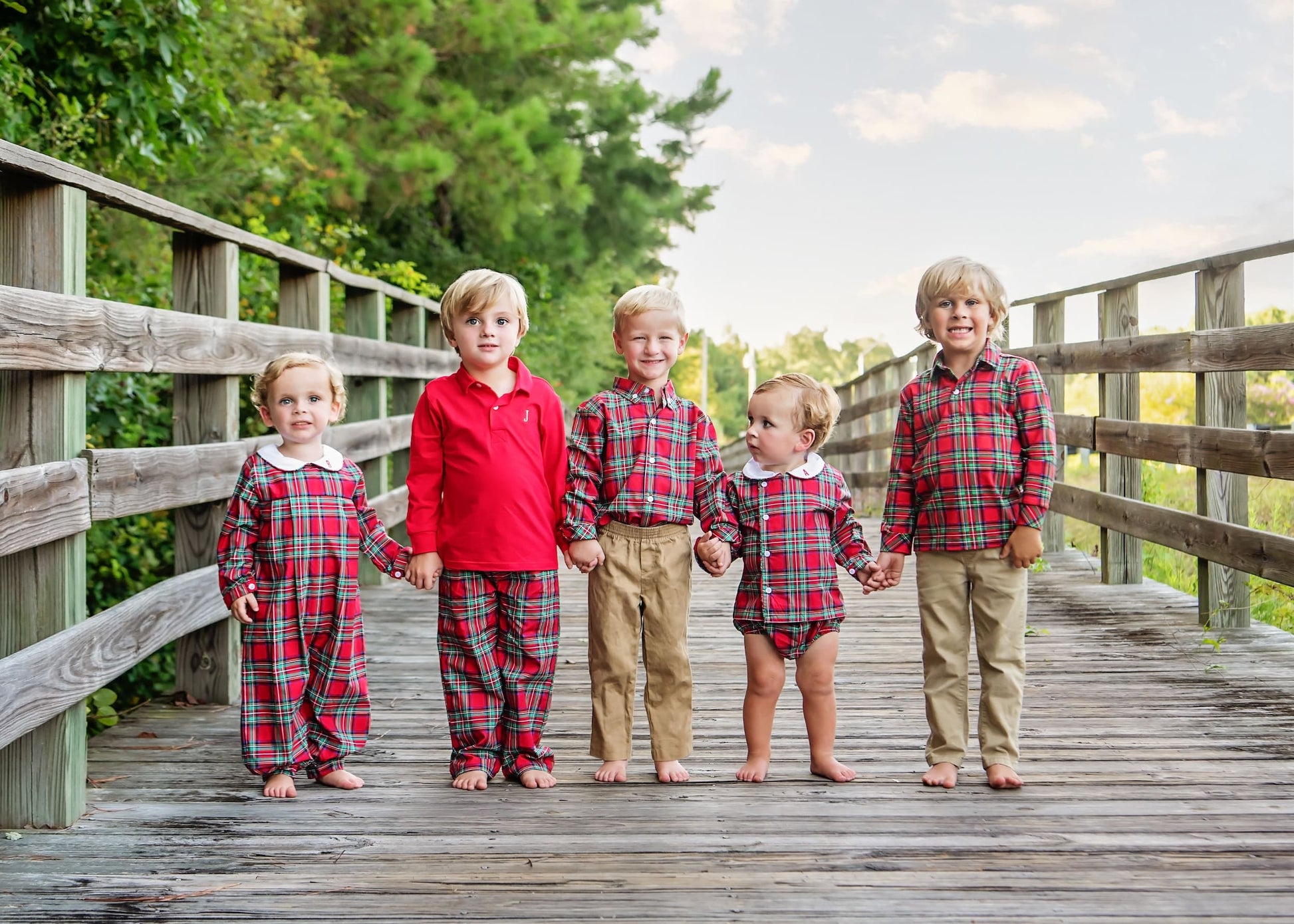 Five children in matching red plaid outfits standing on a wooden bridge.