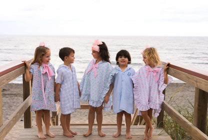 Five children in swimsuits and coverups holding hands on a deck by the ocean