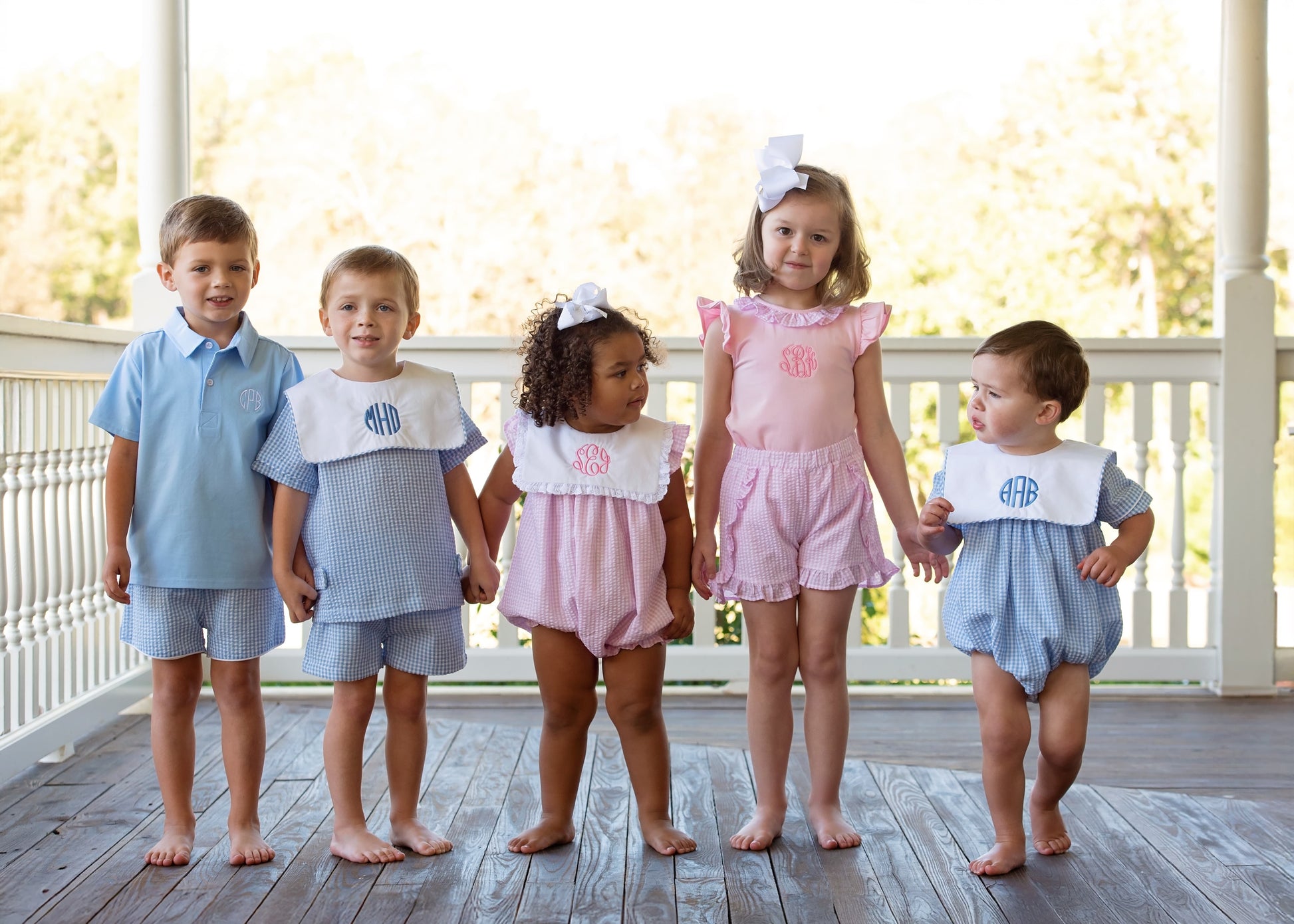 Five children wearing matching seersucker outfits on a wooden deck.