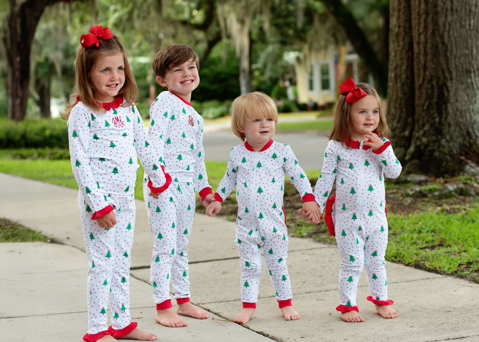Four children in matching Christmas-themed pajamas standing outdoors on a sidewalk.