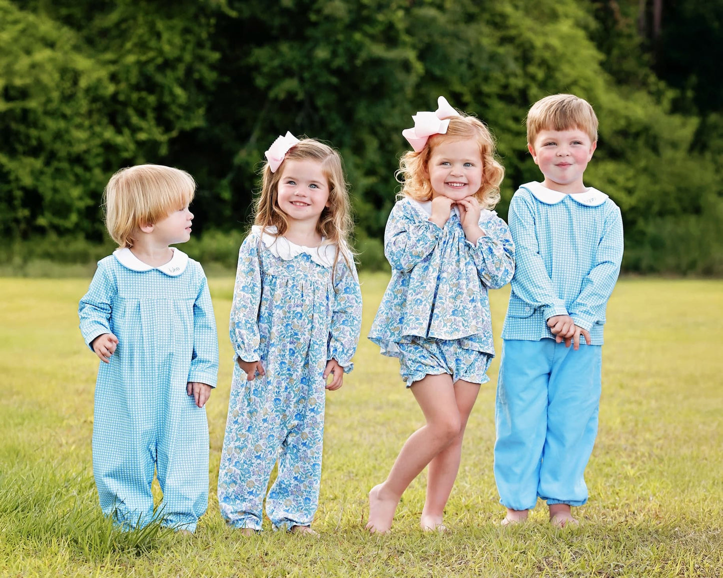Four children in matching blue outfits standing in a grassy field.