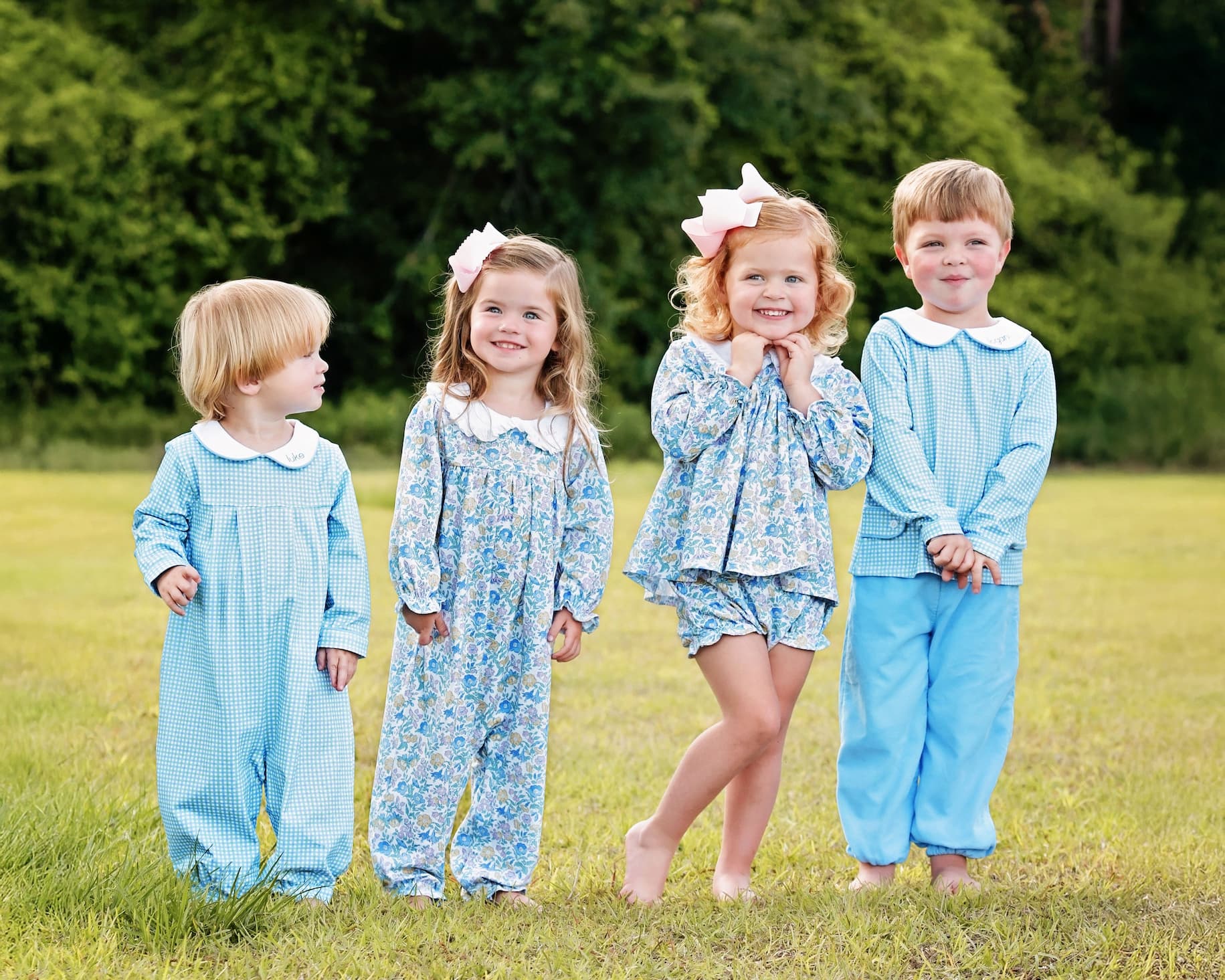 Four children in matching blue outfits standing in a grassy field.