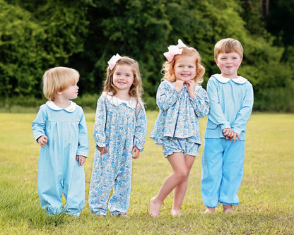 Four children in matching blue outfits standing in a grassy field.