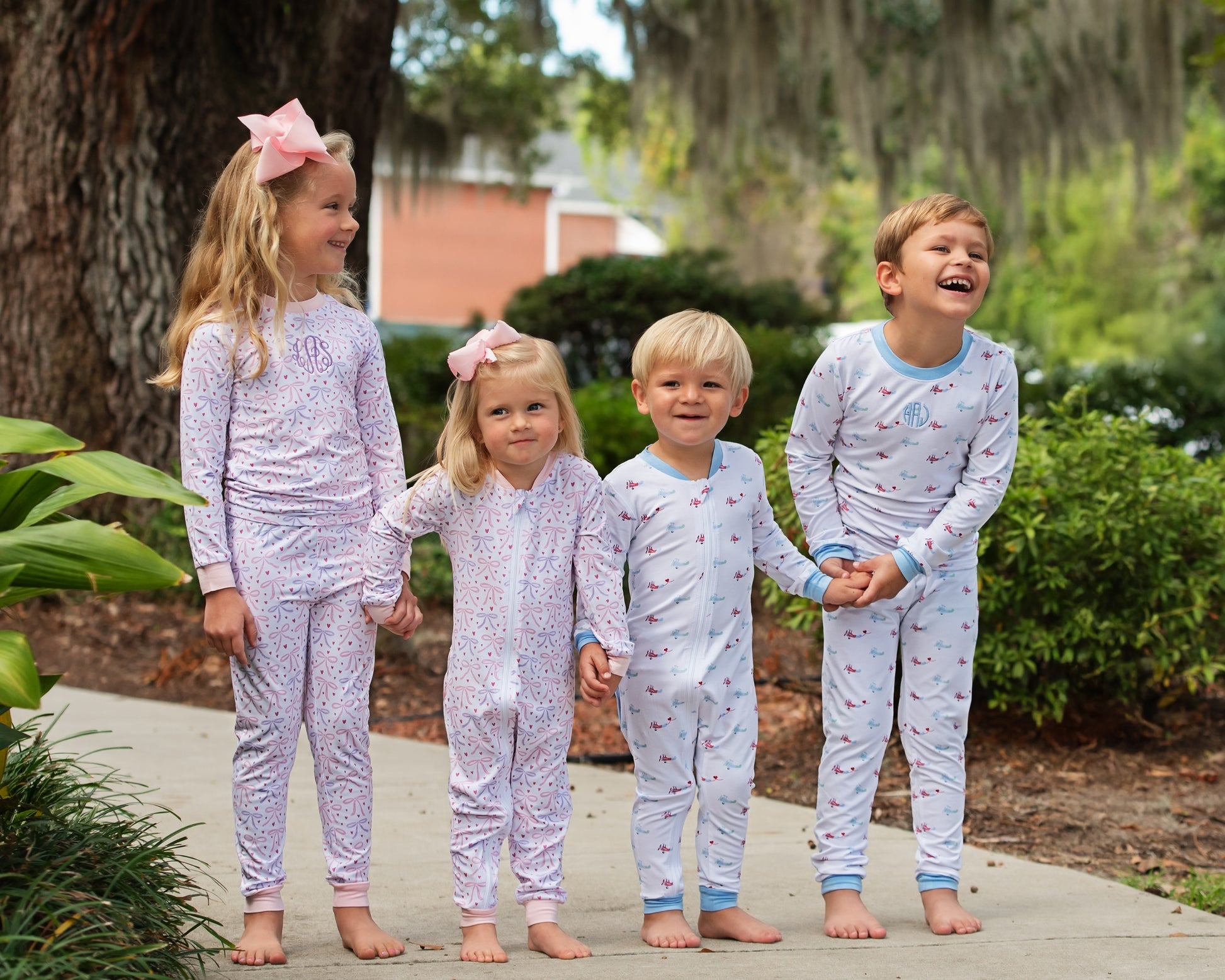 Four children in matching knit pajamas standing outdoors on a sidewalk.