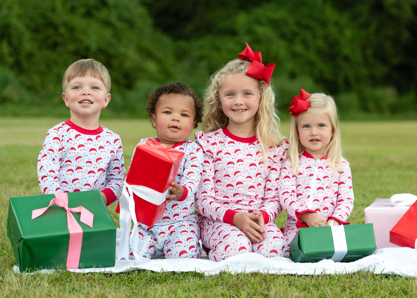 Four children in matching pajamas with Christmas presents on a grassy field.