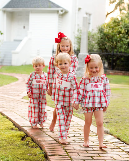 Four children in matching red and white checkered outfits standing on a wooden path outdoors.