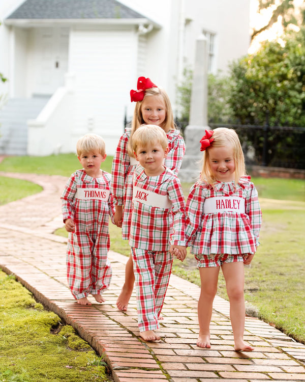 Four children in matching red and white plaid custom smocked outfits on a wooden path