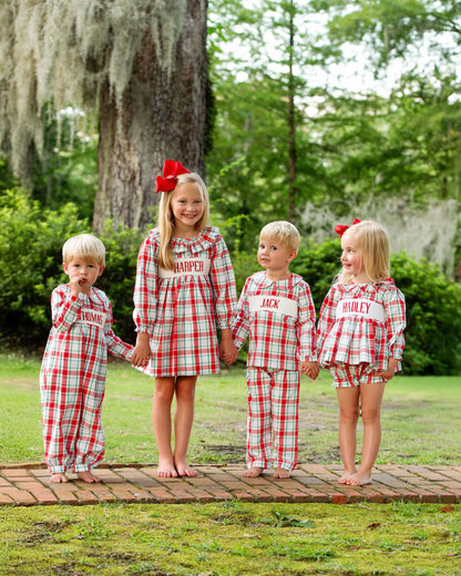 Four children in matching red and white checkered pajamas standing on a wooden platform outdoors.