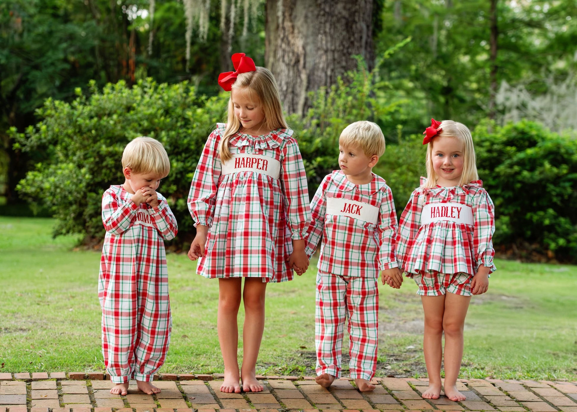 Four children in matching red and white plaid outfits with names on them, standing outdoors.