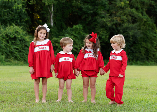 Four children in matching red outfits standing in a grassy field with trees in the background.
