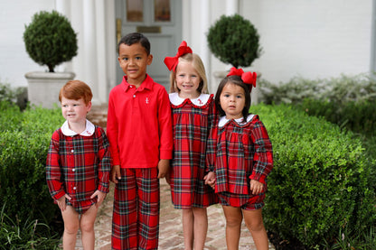 Four children in matching red plaid outfits standing in front of a house.
