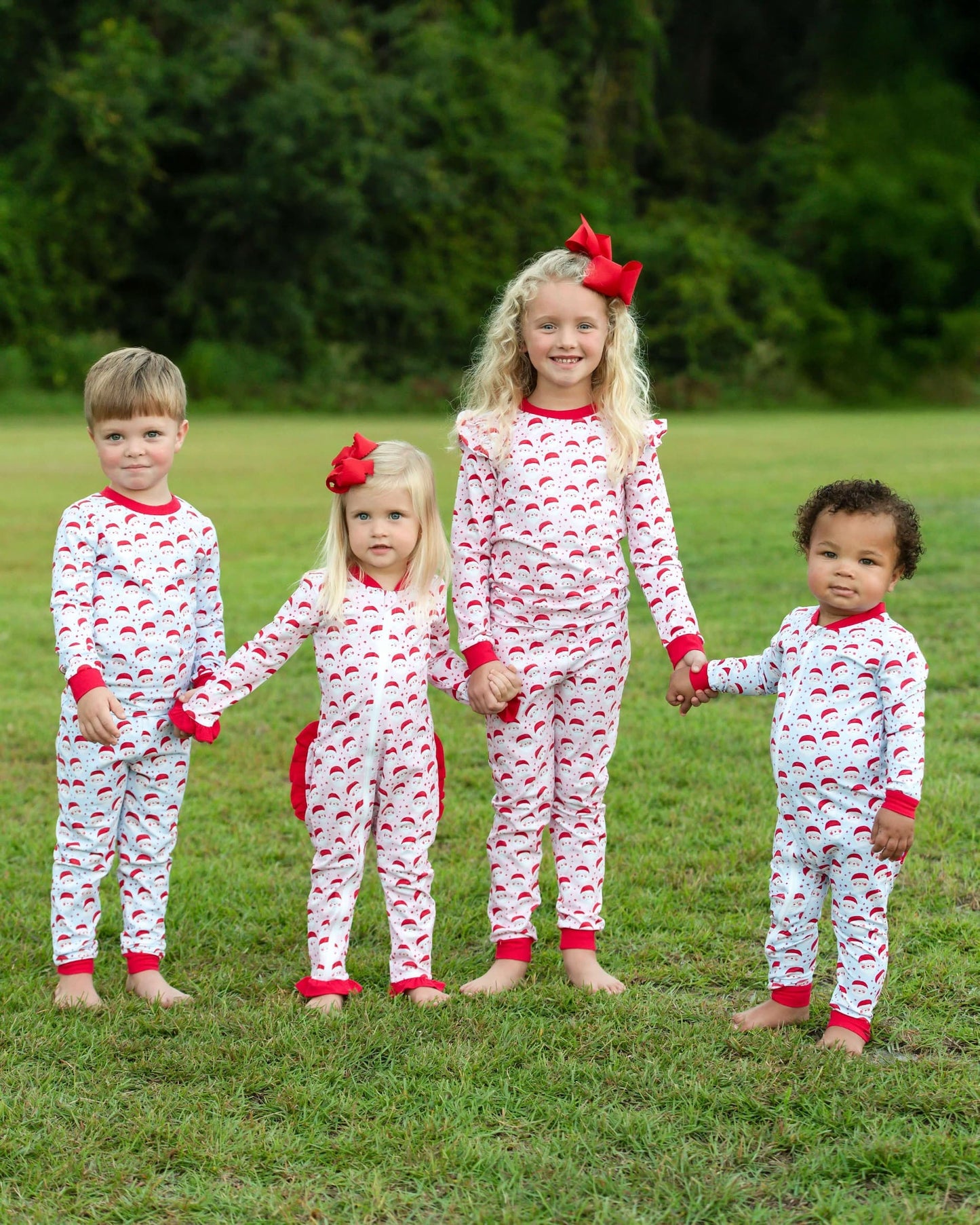 Four children wearing matching pajamas with Santa Clause accents in a grassy outdoor setting.