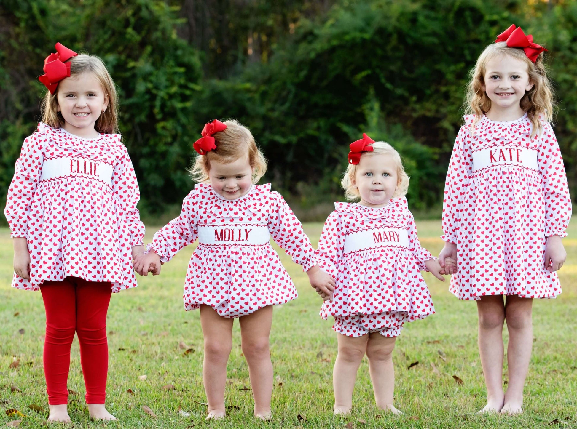 Four girls in matching Valentine outfits with red bows, standing outdoors