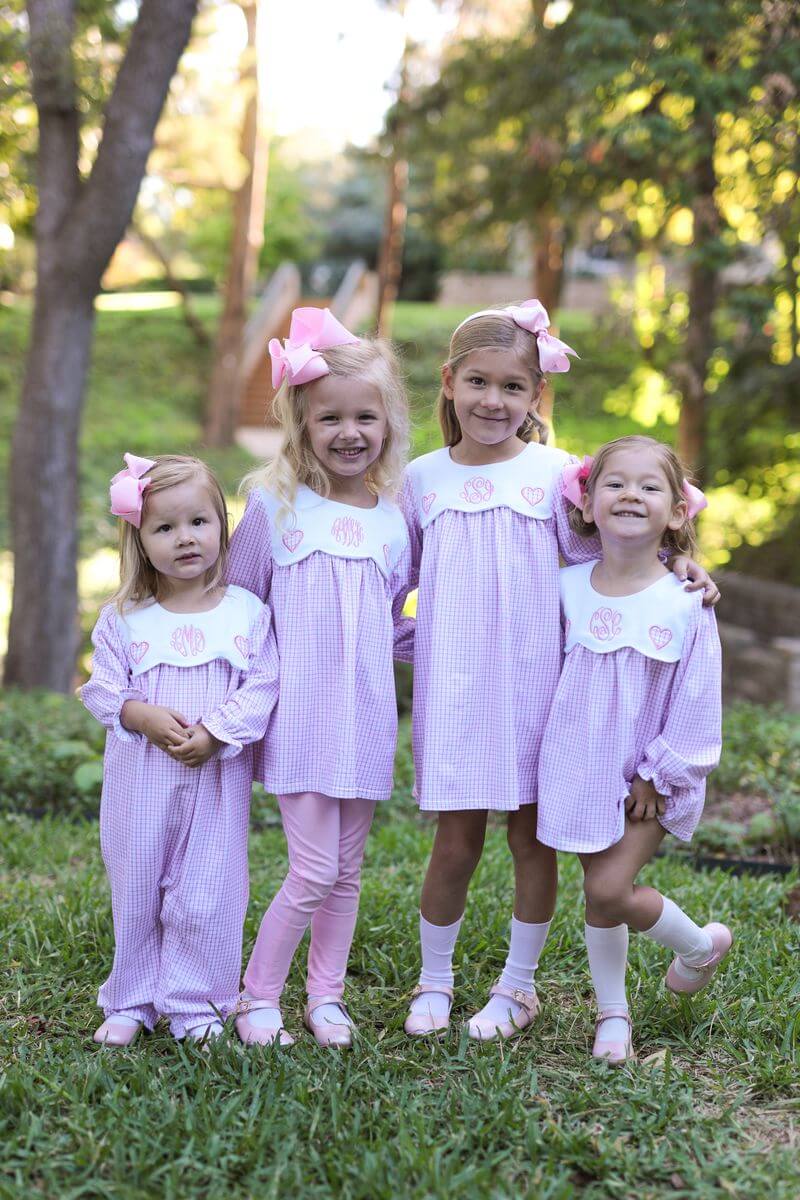 Four young girls in matching dresses standing outdoors with trees in the background