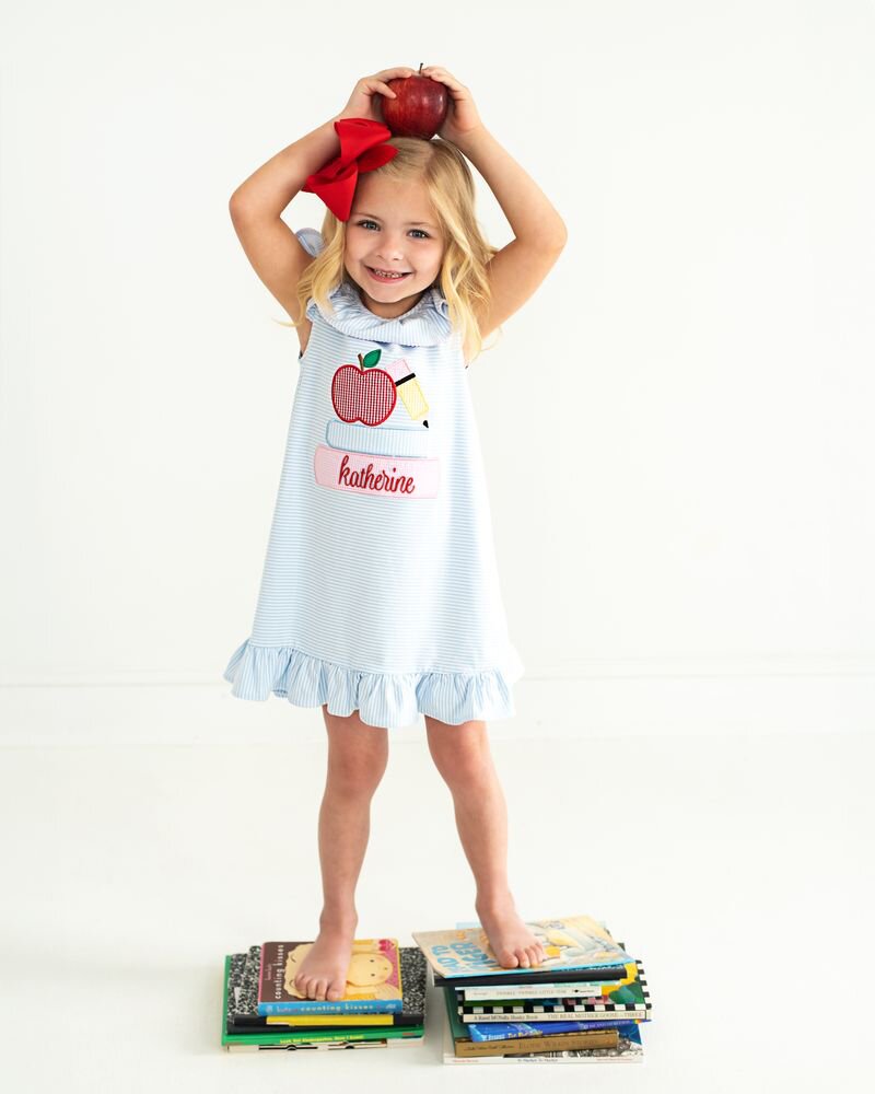 Girl holding an apple over her head, wearing a school dress standing on books. 