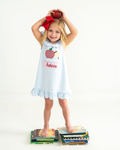 Girl holding an apple over her head, wearing a school dress standing on books. 