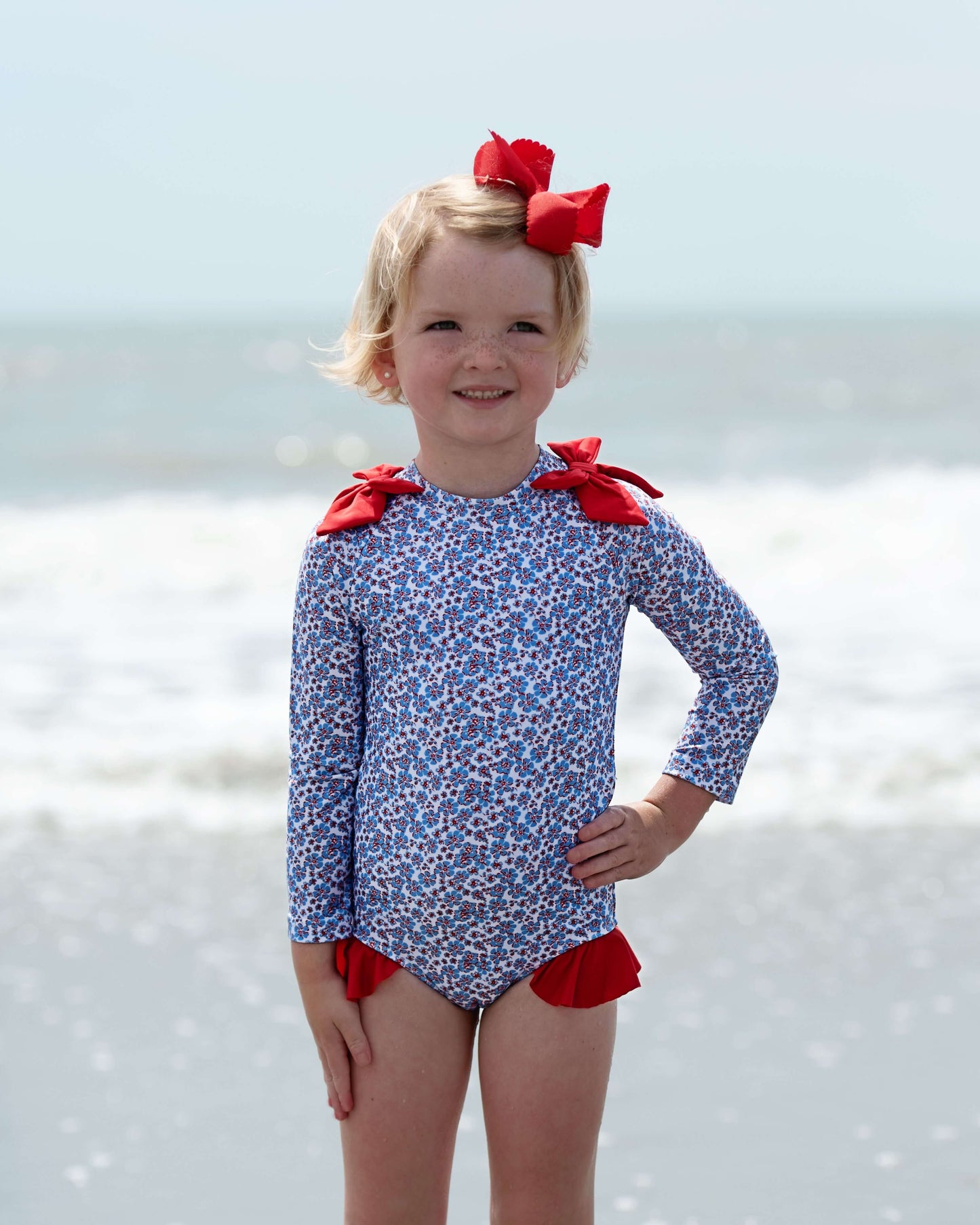 Girl in a floral swimsuit with red bows standing on the beach