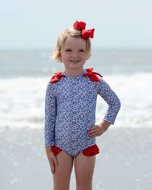 Girl in a floral swimsuit with red bows standing on the beach