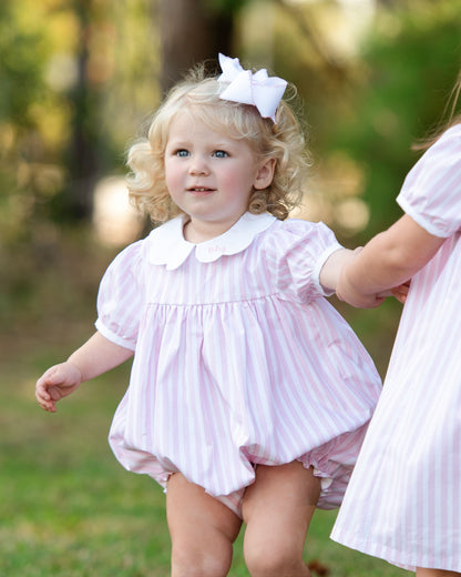 Girl in a pink striped outfit wearing a white bow on her hair standing outdoors