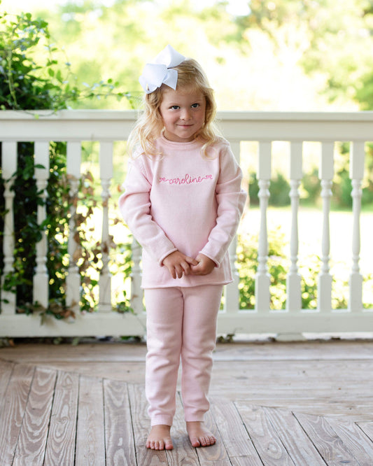 Girl in pink outfit with white bow on her hair standing on a wodden porch