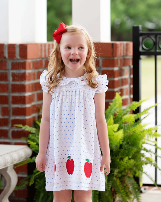 Girl smiling wearing a swiss dot dress with apples and a red bow on her hair. 