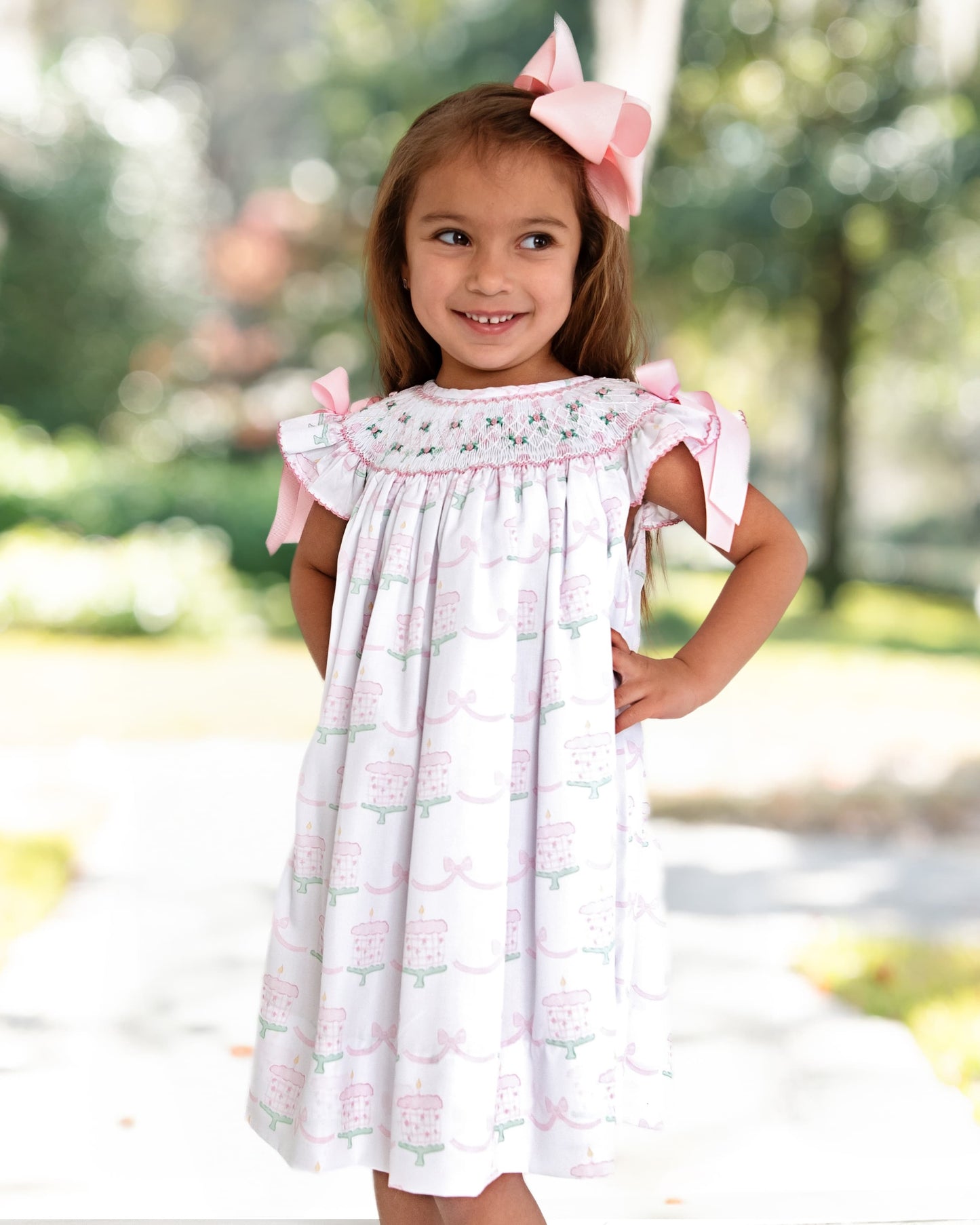 Girl smiling with hands on hips wearing a dress and a bow on her hair