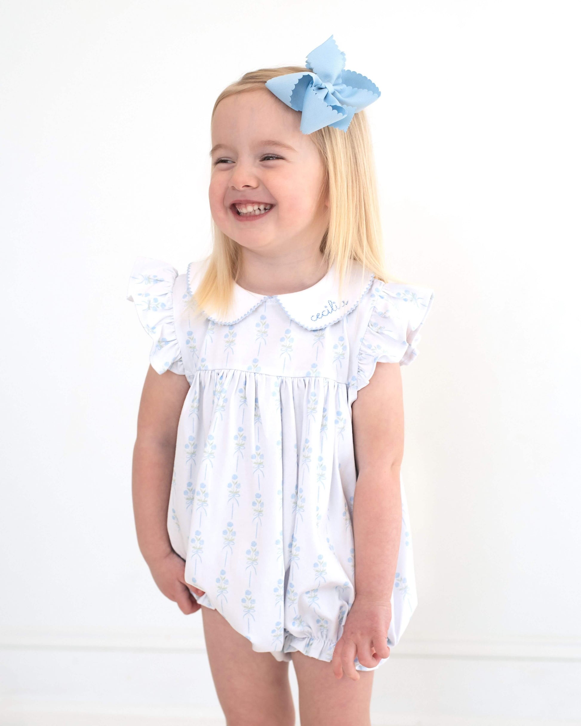 Girl standing in front of white background with a blue bow in her hair