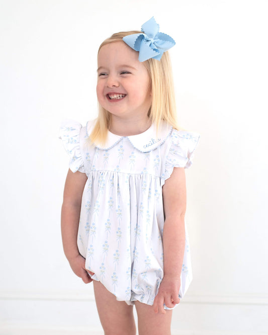 Girl standing in front of white background with a blue bow in her hair