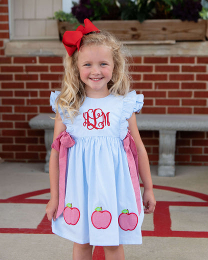 Girl wearing a blue dress with apples and a monogram at the chest.