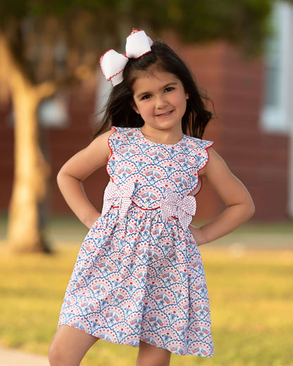 Girl wearing a flag print dress with a white bow on her hair and hands on her hips. 