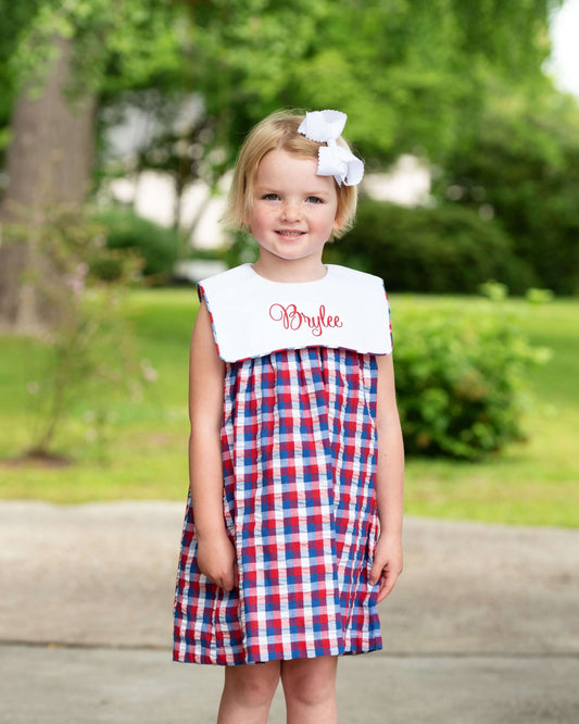 Girl_wearing_a_navy_and_red_checkered_dress_with_white_collar_and_white_bow.