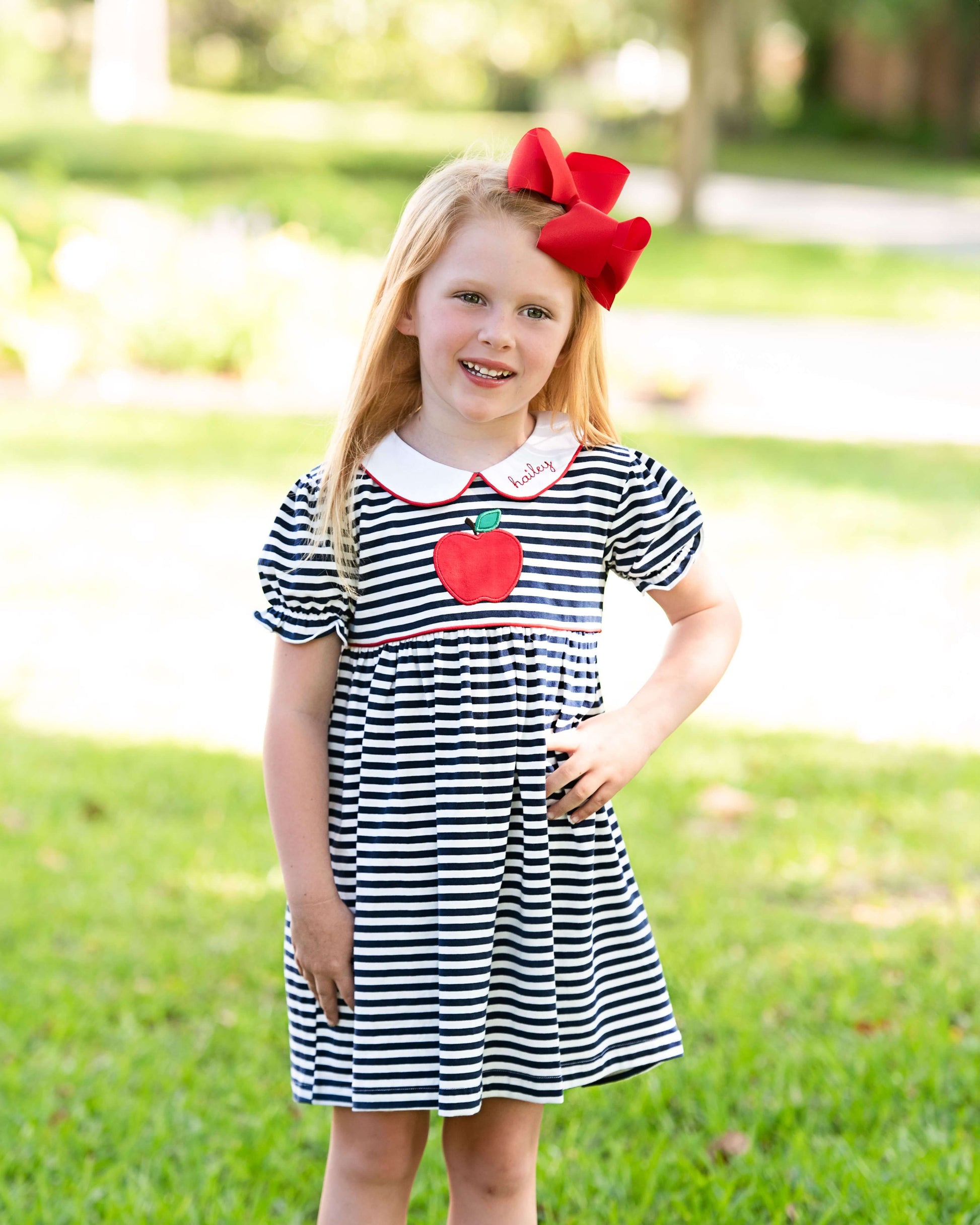 Girl wearing a navy stripe dress with an apple and a red bow on her hair 